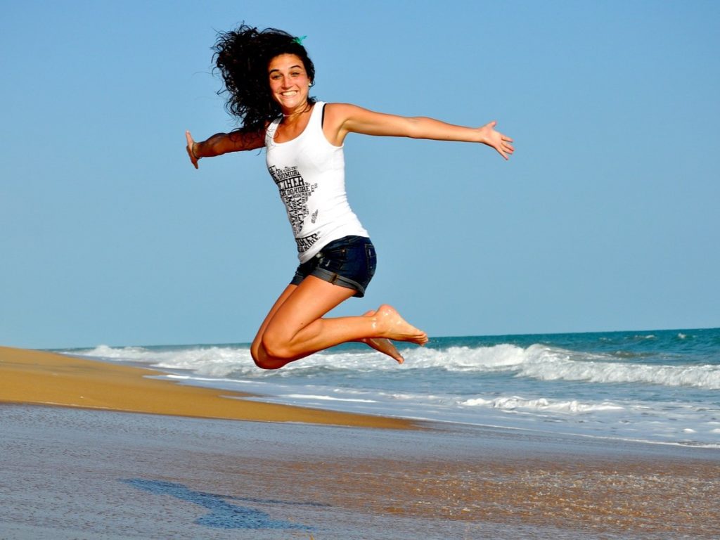 Une femme heureuse, pieds nus sur la place, qui saute en l'air, bien et à l'aise dans son corps.
